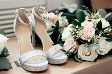 The bride's high-heeled shoes and a wedding bouquet of roses close-up. Wedding traditional accessories in the form of shoes and a bouquet. Sparkling shoes of the bride and a luxurious bouquet