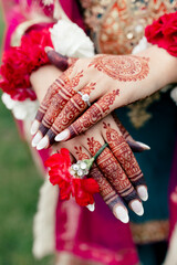 The hands of the Indian bride are decorated with flowers and curly red patterns in the form of traditional ornaments. Beautiful drawings in the Indian style of henna on the hands of the bride close-up