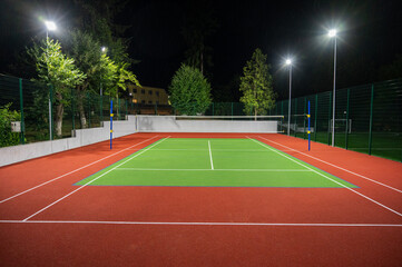Naklejka premium Sports volleyball field in the park with artificial grass of the stadium on the background of green trees. evening lighting with powerful lanterns, view from below