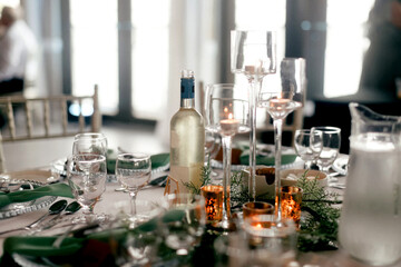 A bottle of white wine and glass goblets on a table in a restaurant. Table setting for receiving guests in a restaurant. Beautifully decorated table in a restaurant with candles and plants