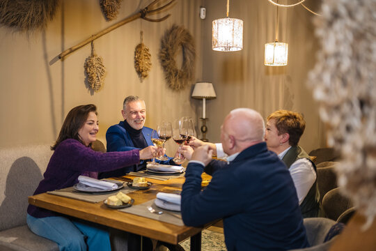 Happy senior friends clinking wineglasses during dinner