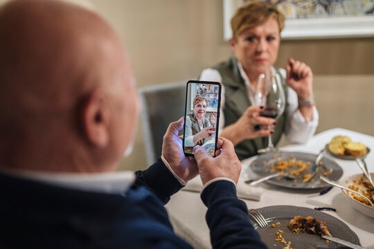 Unrecognizable man taking picture of wife during dinner