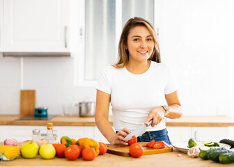 Cheerful young Hispanic woman following healthy diet preparing vegetable salad for dinner in home kitchen