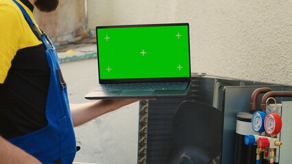 Experienced worker ordering new internal parts on green screen laptop for malfunctioning condenser after finishing review. Seasoned wireman looking online for air conditioner replacement components