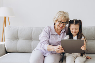 Family, generation, technology - smiling granddaughter and grandmother with tablet pc computer...