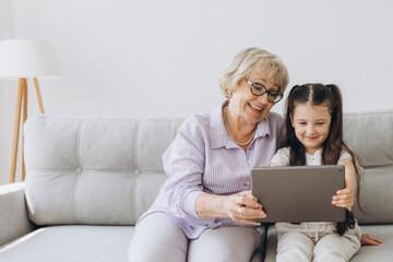 Family, generation, technology - smiling granddaughter and grandmother with tablet pc computer...