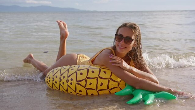 A girl with sunglasses is relaxing and enjoying a vacation on a colorful inflatable circle in the shape of a pineapple. The atmosphere of holiday and recreation.