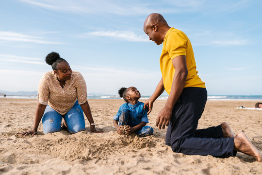 Black family and daughter playing with sand at beach
