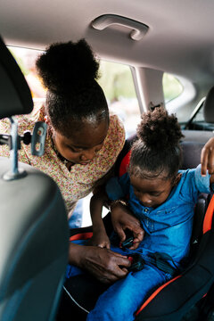Mother fastening belt on daughter in back seat
