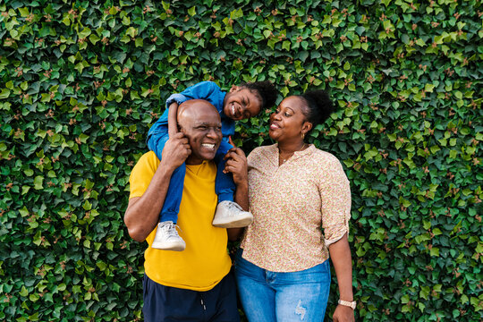 Cheerful family with girl near green wall at park