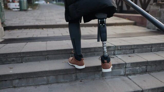 Artificial limb, Determined step, Orthotic support. Man with prosthetic leg due to disability ascends stairs on city street.