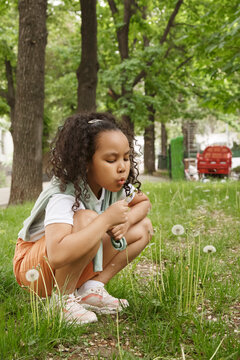 Cute girl blowing dandelion flower in park