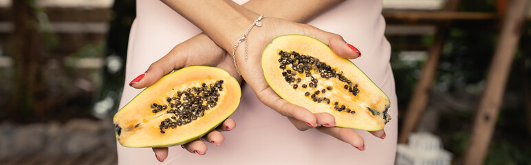Cropped view of young african american woman in summer dress holding cut papaya while standing in garden center, trendy woman surrounded by tropical lushness, banner, summer concept