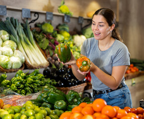 Obraz premium Young woman chooses bell pepper for purchase in vegetable shop
