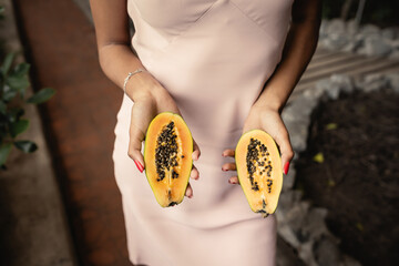 Cropped view of trendy young african american woman in summer dress holding fresh cut papaya while standing in garden center, fashion-forward lady inspired by tropical plants, summer concept