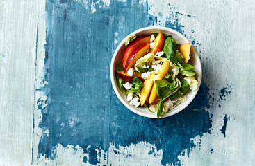 Summer nectarine salad with green leaf vegetables and feta on wooden painted background. Top view