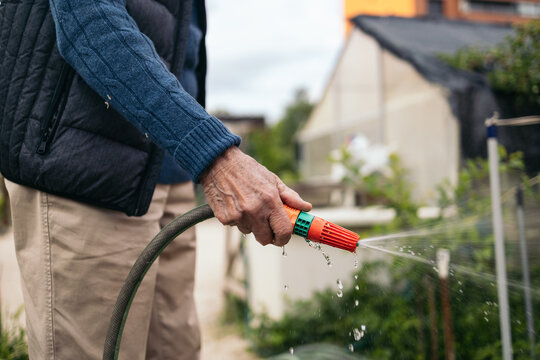 Unrecognizable senior man watering plants in an urban garden