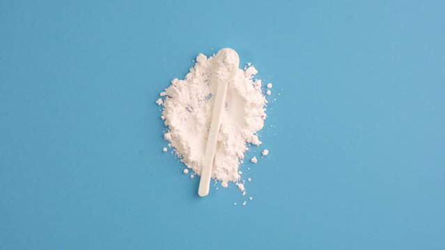 Pile of Titanium dioxide and measuring spoon on blue background, top view. TiO2, White chemical powder. Food additive E171. Titanium dioxide used in cosmetic, medicine, and skin care products.