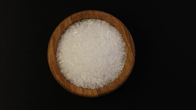 Monosodium glutamate, MSG powder in wooden bowl, top view. Chinese salt, food additive E621 used in food industry. Fifth taste, umami. Palatability enhancer. Oblong white crystalline granules.