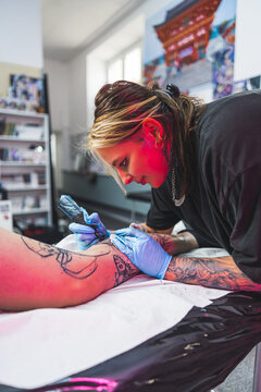 nice-looking professional tattooist girl making a new tattoo on a leg in her studio, vertical shot. High quality photo