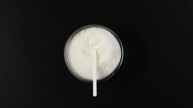 Tartaric acid powder in bowl with measuring spoon on dark background, top view. Video 4K. Rotating, clockwise. Food additive E 334. Salt, potassium bitartrate, known as cream of tartar.