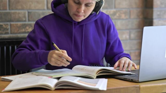 female student figure studying open textbooks on table, reading writes notes pen, laptop headphones. brown interior. concept back to school, distance learning, homework knowledge report, work, exams