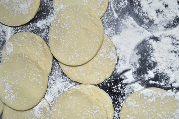 cut dough for dumplings in flour lies on a black table
