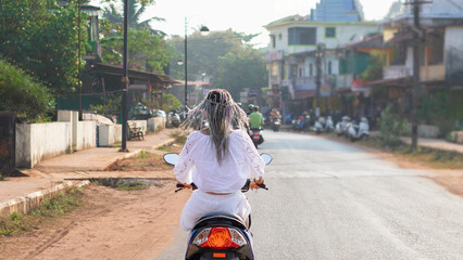 woman in white clothing is riding a scooter through the streets of Asia
