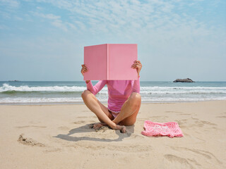 Woman covering her face with a pink book on the beach