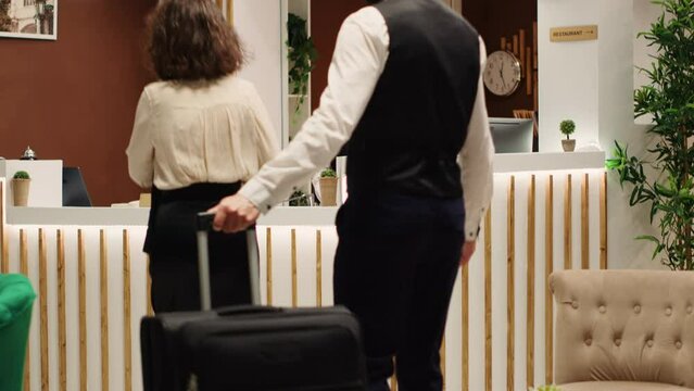 Guest arrives in hotel lobby, helped by bellboy with luggage and by asian receptionist with accommodation registration. Teamworking friendly helpful resort staff assisting tourist during check in