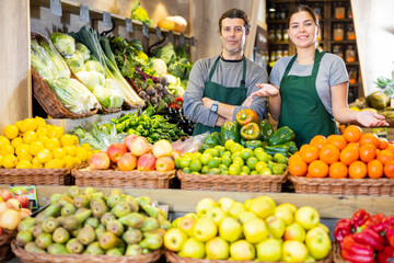 Male and woman salespeople standing near market stalls offering to buy fruits and vegetables