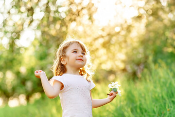 Happy little girl child having fun raising her hands up in sunny summer day