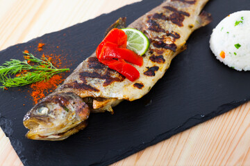 Image of tasty baked whole trout with rice, served with lemon and greens at plate