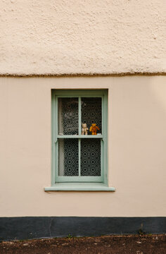 2 tiny teddy bears in the window of a house.