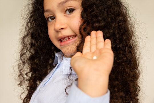 Little girl looking at the camera and showing the tooth she has lost. 