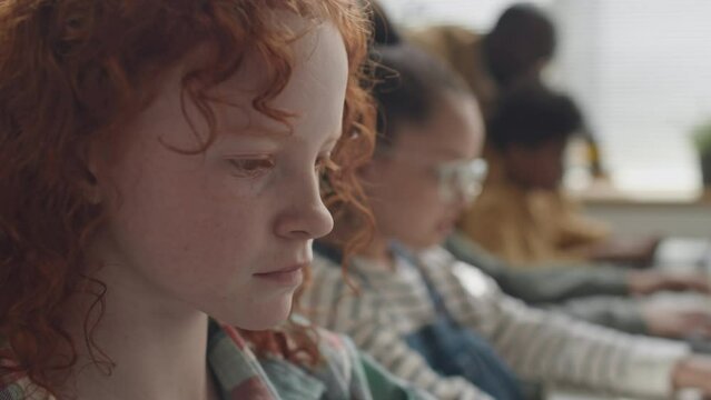 Close up shot of face of thoughtful school girl with red hair coding during computer class