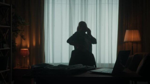 A woman walks around the room and speaks on the phone. A woman holds a blouse on a hanger in her hand, examines it. A woman is going to a meeting. Dark silhouette of a woman in the living room.