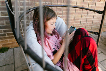 Tween girl sits on swing chair and texts on her phone