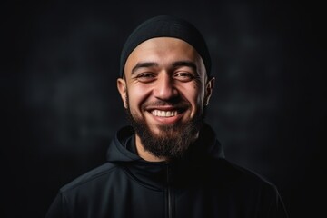 Portrait of a smiling bearded man in a black hoodie on a dark background