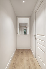 A long corridor of a house with a light wooden floor with access doors to the rooms