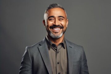 Portrait of a handsome middle-aged Indian man smiling at the camera while standing against grey background