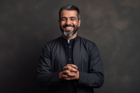 Portrait of a smiling bearded Indian man in a black shirt.