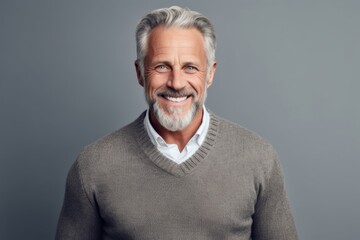 Obraz premium Portrait of a smiling senior man with grey hair and beard standing against grey background