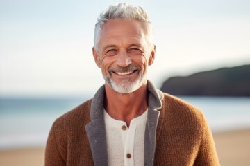 Fototapeta na wymiar Portrait of smiling senior man standing on beach and looking at camera