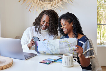 Two Black women friends planning a vacation trip with phone and 