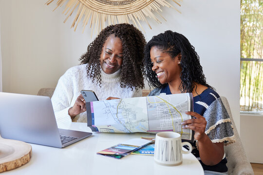 Two Black women friends planning a vacation trip with phone and 