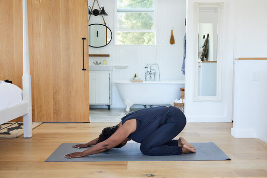 Mature Black woman in child pose doing yoga at home