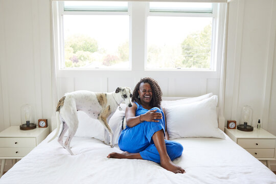Mature Black woman laughing with her dog on her bed at home