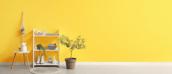Shelving unit with female clothes and accessories near yellow wall. Banner for design