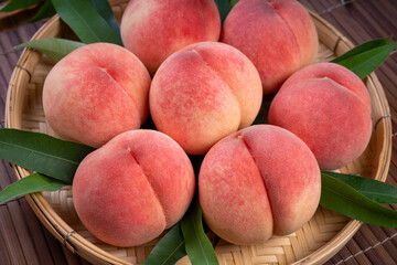 Peaches with leaves on the wooden table, Fresh pink Peach wooden basket plate in wooden Background.